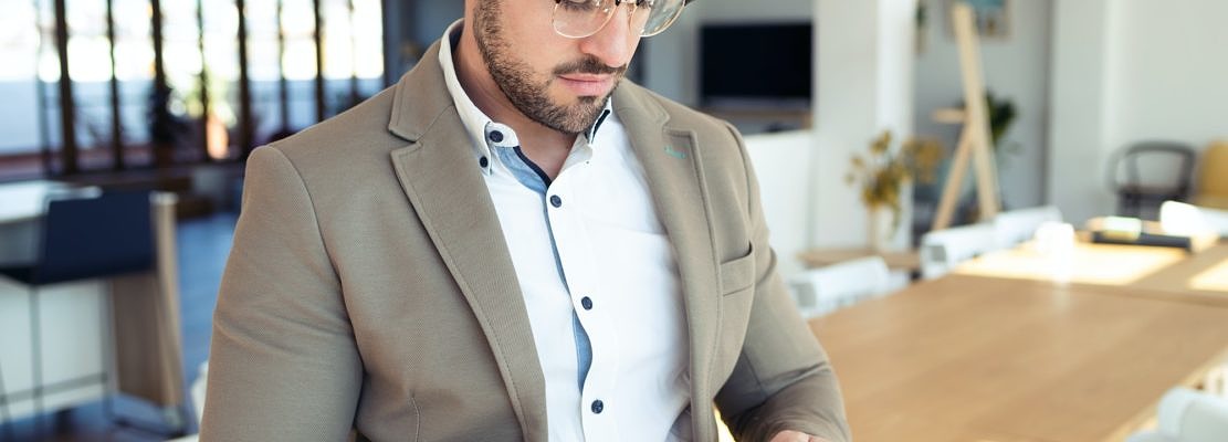 Handsome young business man using his smartphone while sitting on table in the office.