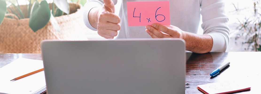 teacher showing multiplication flash card and thumbs up to student on computer during online lesson