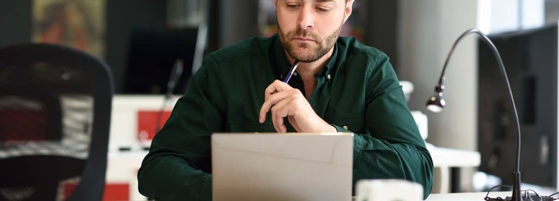 Young man studying with laptop computer on white desk.