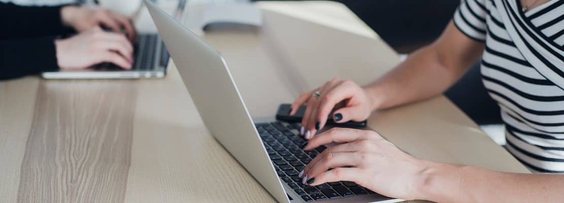 Close up picture of hands of two businesswomen typing on their tablet computer and laptop.