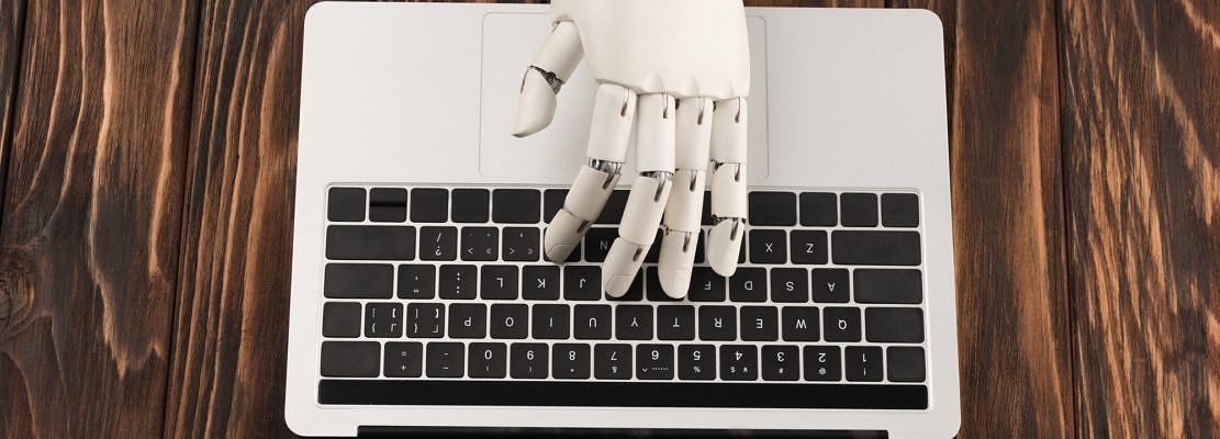 cropped shot of robot working with laptop on wooden surface