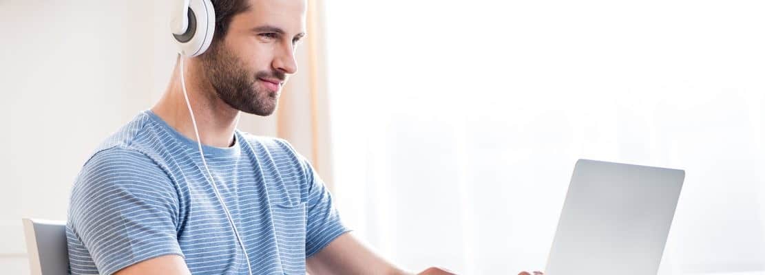 Young smiling man in white headphones using laptop