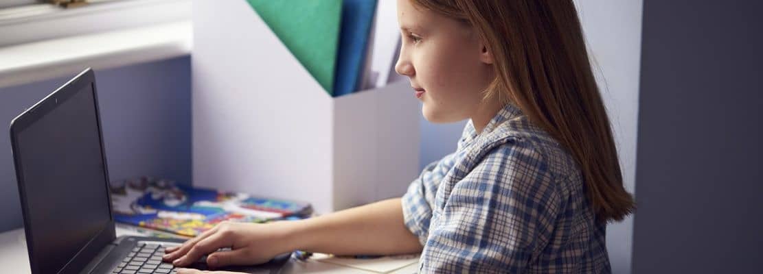Girl Sitting At Desk Home-Schooling Using Laptop For Online Learning During Health Pandemic