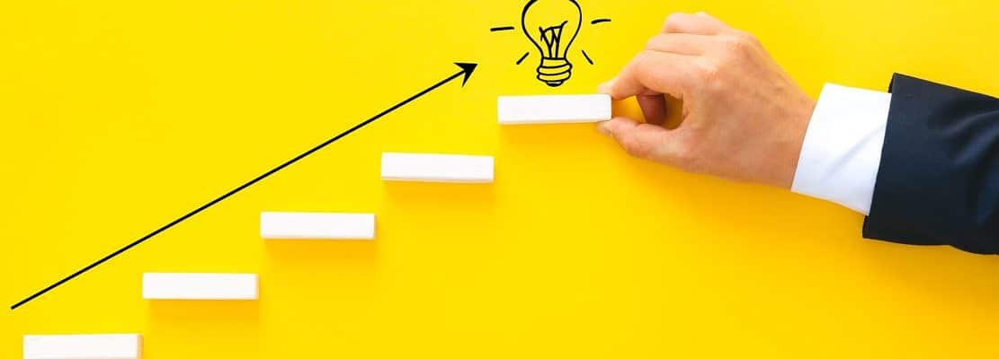 Businessman hand arranging wood block stacking as step stair with lightbulb. Business start-up goals