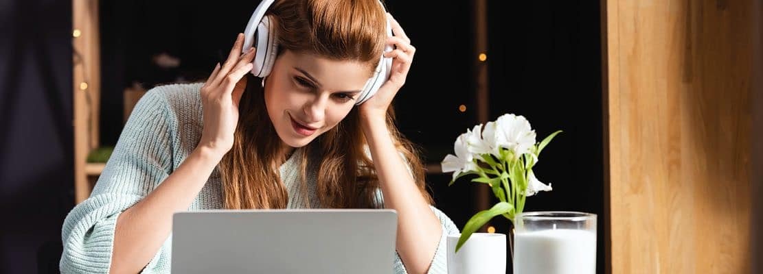 woman in headphones watching webinar on laptop in cafe