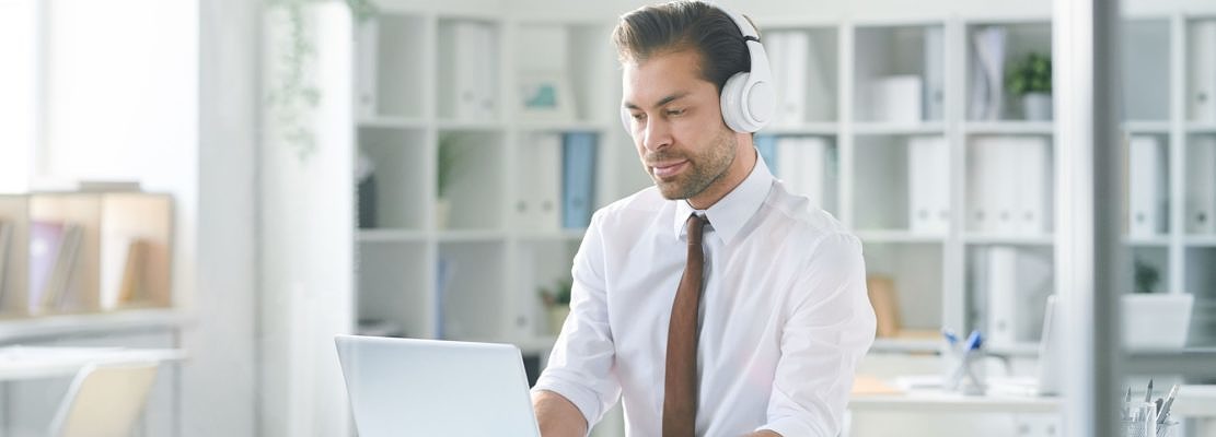 Young concentrated businessman in headphones typing on laptop keypad