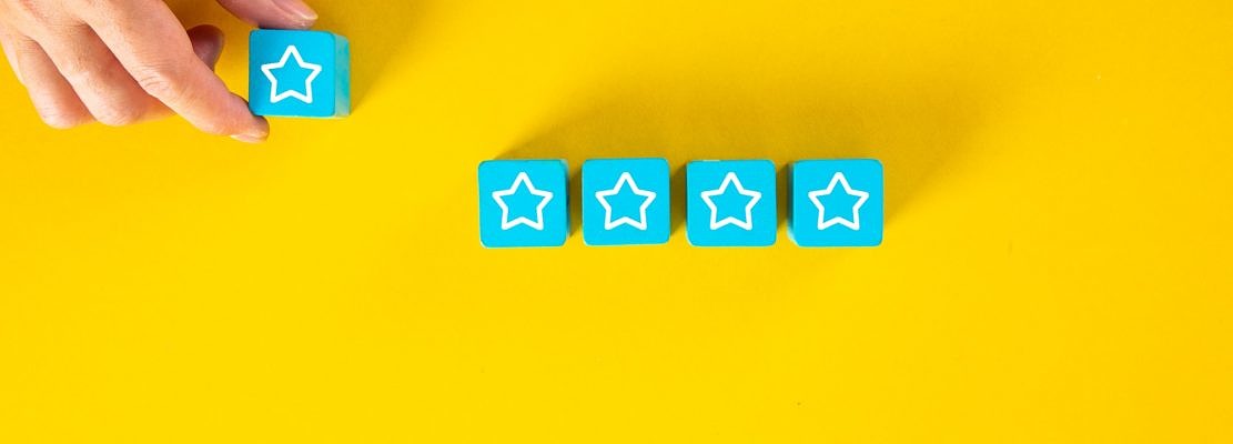 Male hand placing wooden cubes with five star rating on yellow background.