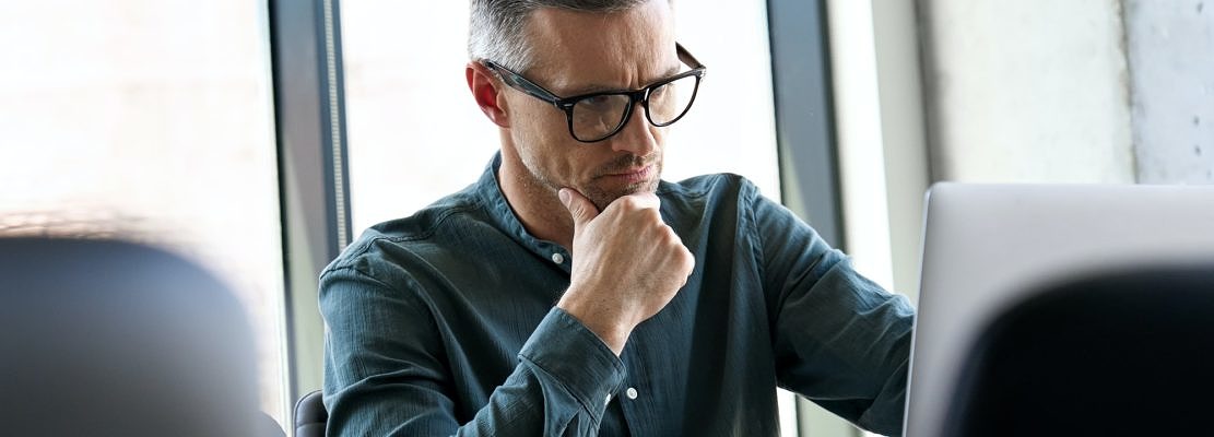 Serious busy mature businessman thinking using laptop sitting at office table.