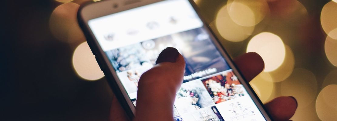 Mobile phone with Instagram social media images on the screen and bokeh lights in the background