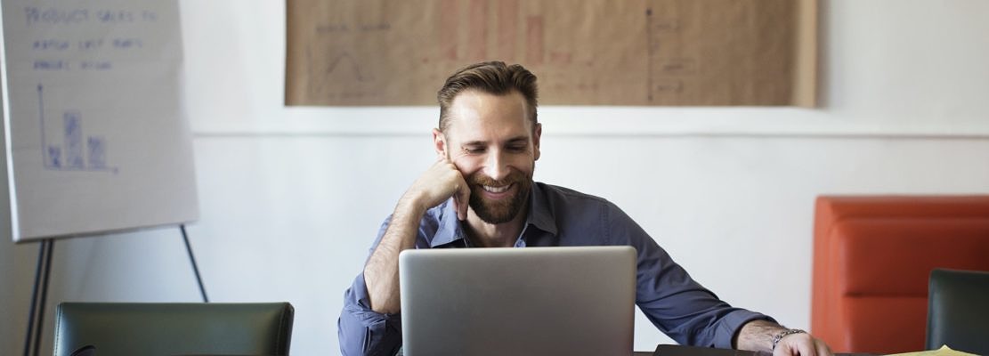 Smiling Businessman Looking At Laptop Computer While Sitting In Office