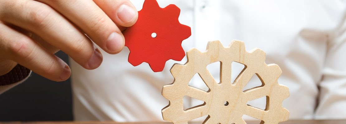 Businessman connects a small red gear to a large gear wheel.