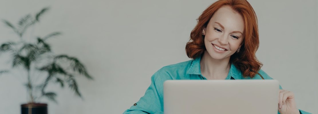 Happy ginger woman freelancer works on laptop computer at home, studies online, uses software