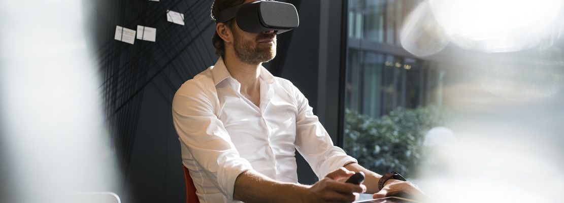 Business man with virtual reality glasses and tablet sitting in modern office