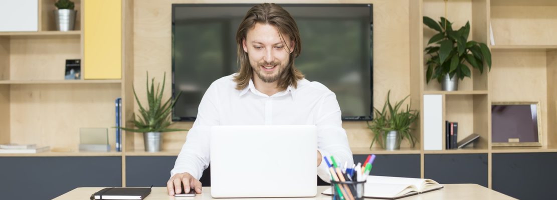 Casually dressed young businessman working on a laptop while sitting at a desk in an office