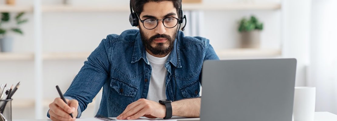 Millennial arab guy in headset watching online webinar on laptop at home, studying with computer and