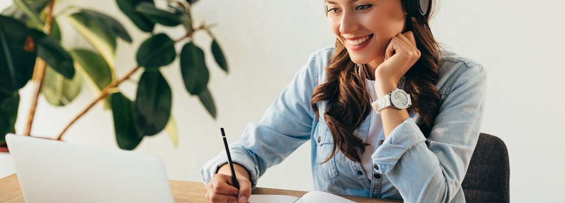 portrait of young smiling woman in headphones taking part in webinar in office