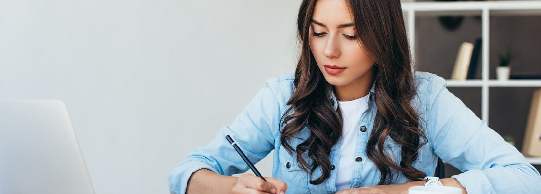 young woman at tabletop with laptop taking part in webinar in office