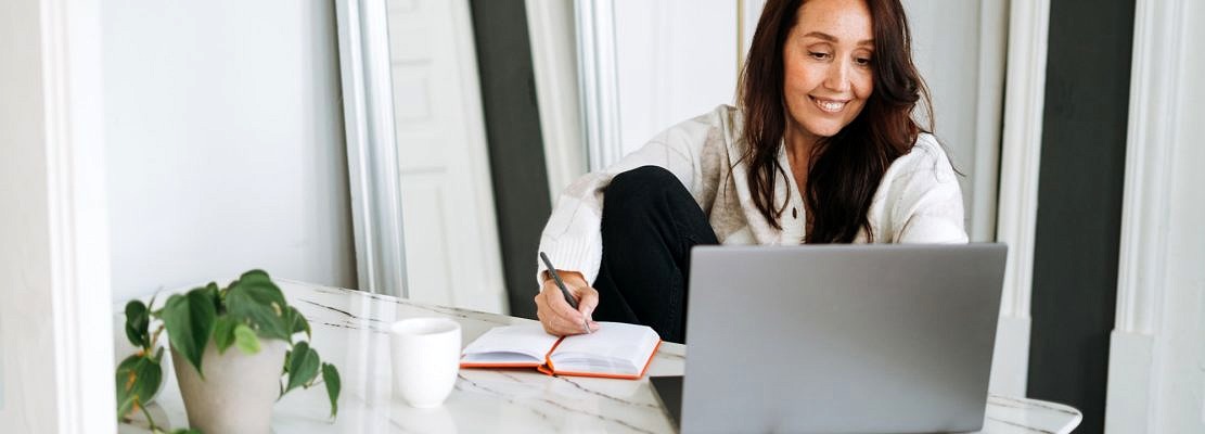 Smiling brunette woman with long hair in white cardigan working on laptop in bright modern office