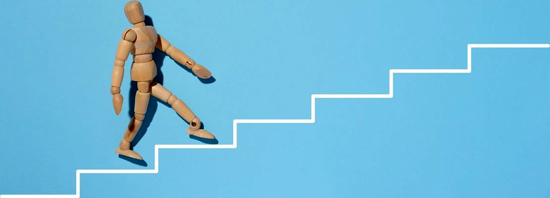 A wooden mannequin goes up a painted white staircase on a blue background.