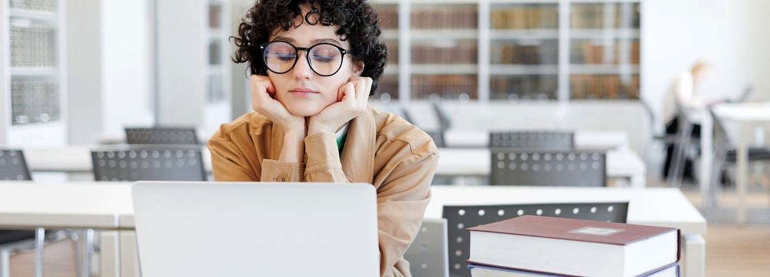 thoughtful woman works in library, watches an educational webinar on Internet, is bored. coworking