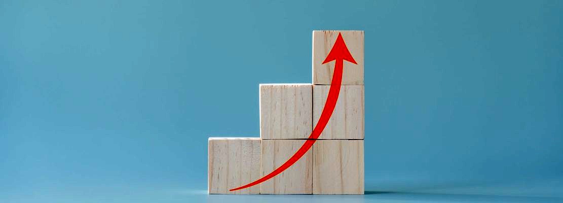Red arrow going up on wooden blocks and light blue background
