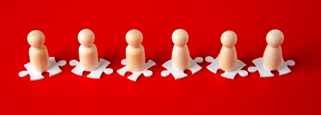 Wooden figures on puzzles on red background as a symbol of team building.