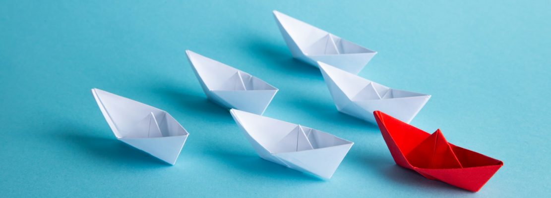 Red leader paper ship leading among others on blue background. Leadership concept.