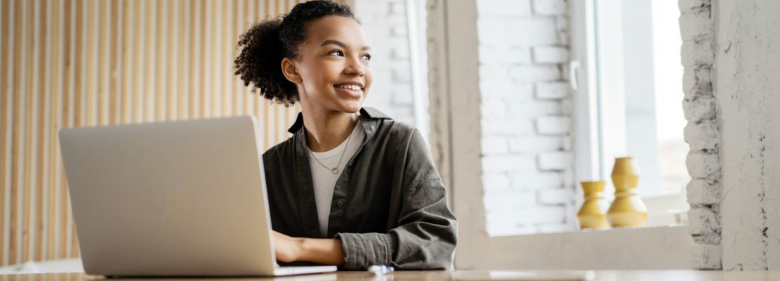 Smiling young woman working on laptop in a modern loft space, embodying productivity