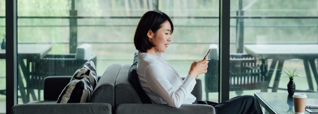 Asian businesswoman texting with smartphone at office window