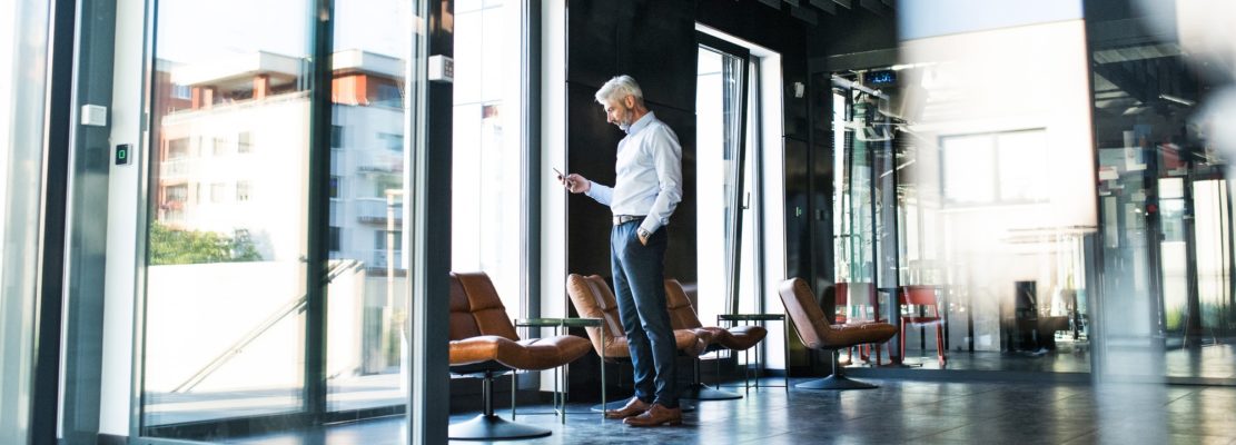 Mature businessman with smartphone in the office.