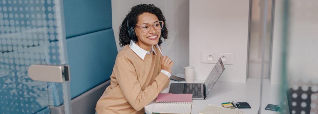 Stylish business woman in eyeglasses and headphones working on laptop while sitting in office