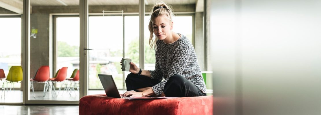 young businesswoman working in modern office, sitting on stool, using laptop