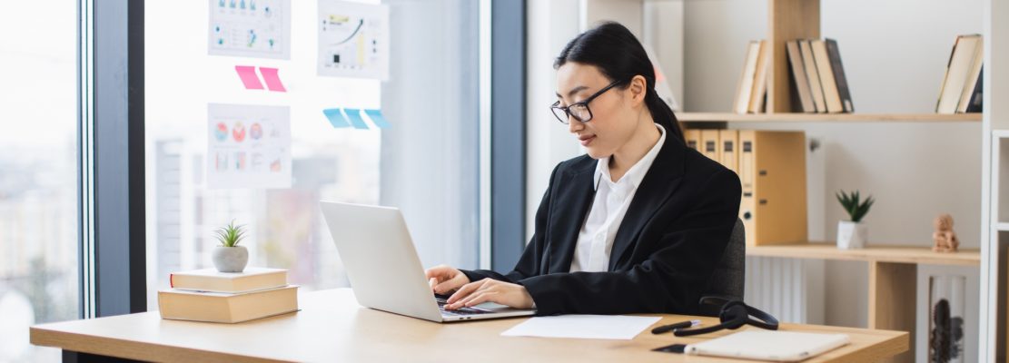 Asian businesswoman working on laptop in modern office setting