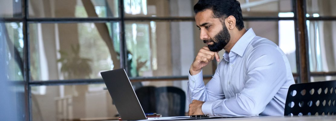 Indian businessman using laptop computer working in office looking at laptop.