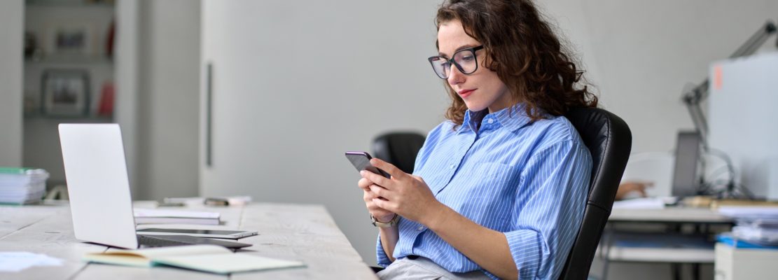 Young business woman using smartphone working in office sitting at desk.