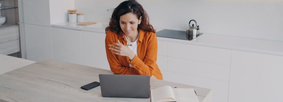 Female freelancer in earphones communicates via laptop video call, working from home. Distant work