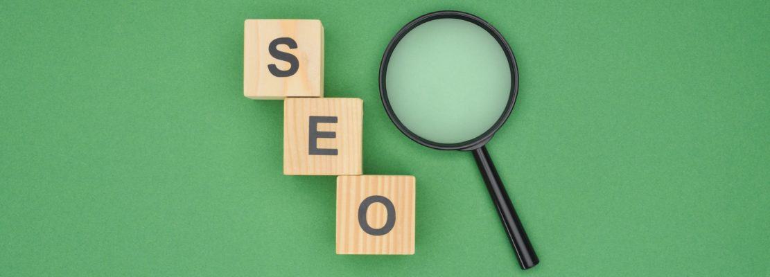 Top view of wooden cubes with seo lettering and magnifier glass on green background