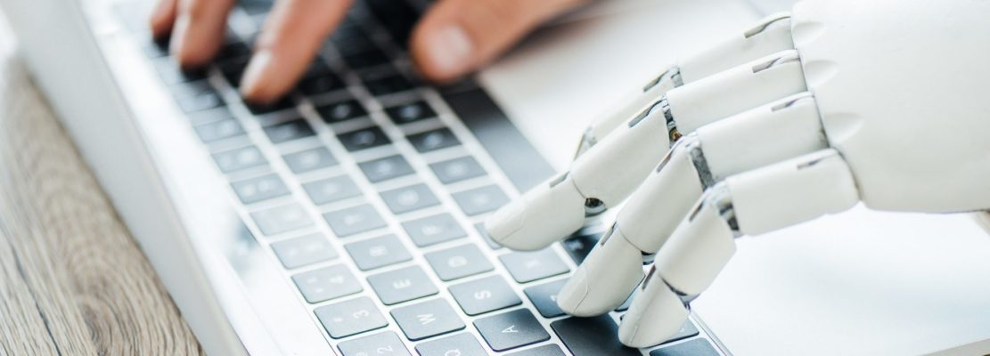 close-up view of human and robot hands typing on laptop at workplace