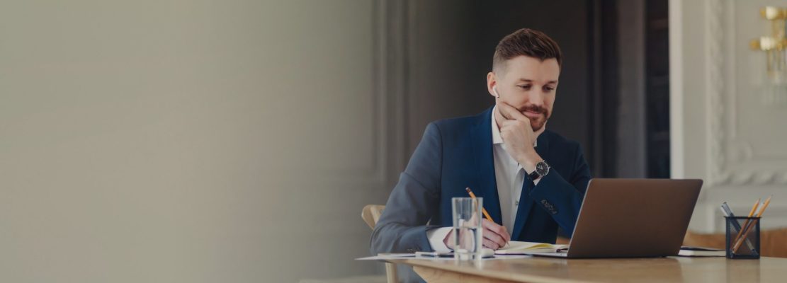 man makes notes in notebook concentrated at laptop screen listens training webinar
