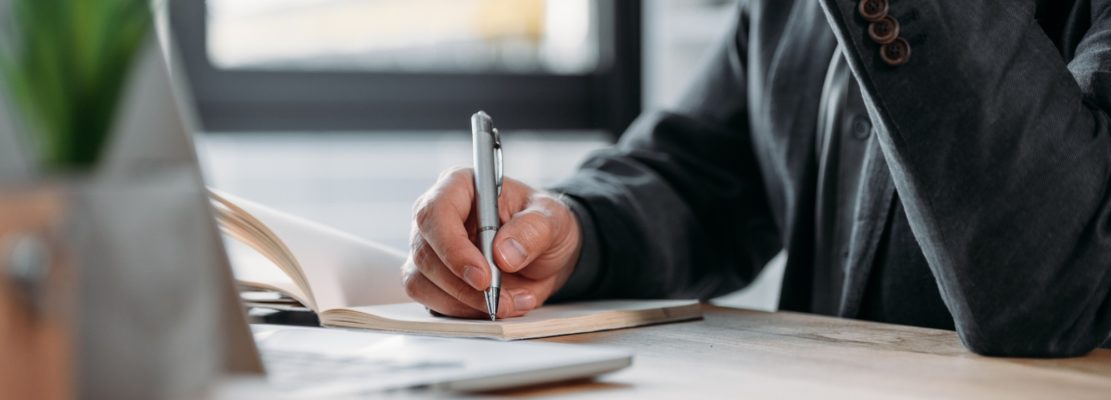 close-up partial view of businessman taking notes in notebook at workplace