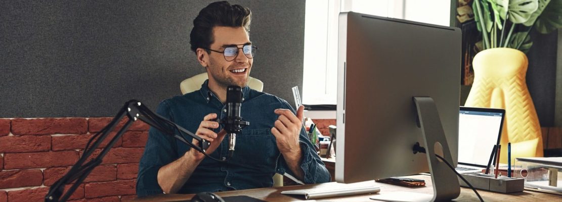 Handsome young man using microphone and gesturing while recording podcast in studio