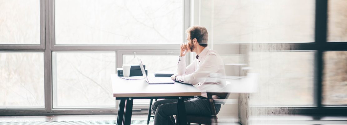 Young business man sitting at table looking at the window and thinking at modern office.